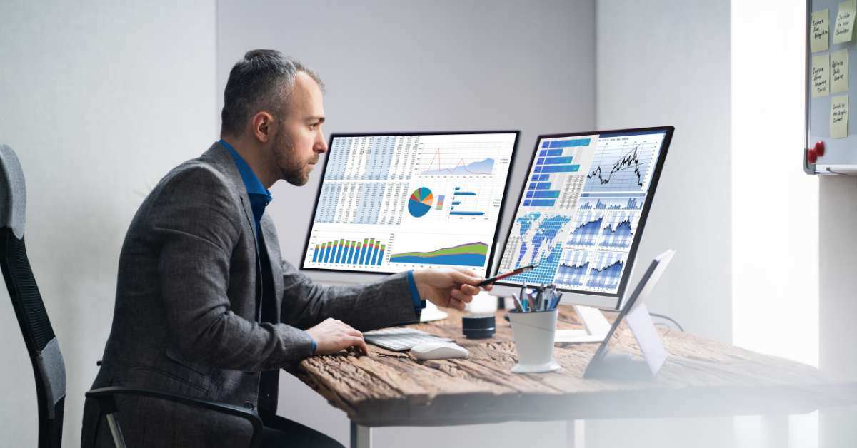 Man sits at a computer chair viewing a screen filled with data reports