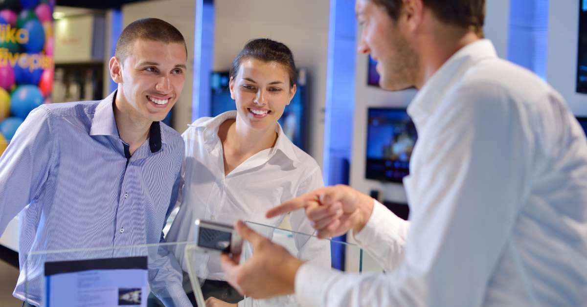 Retail customers review an electronic product with a cashier that uses GenAI to record customer interaction and data. 